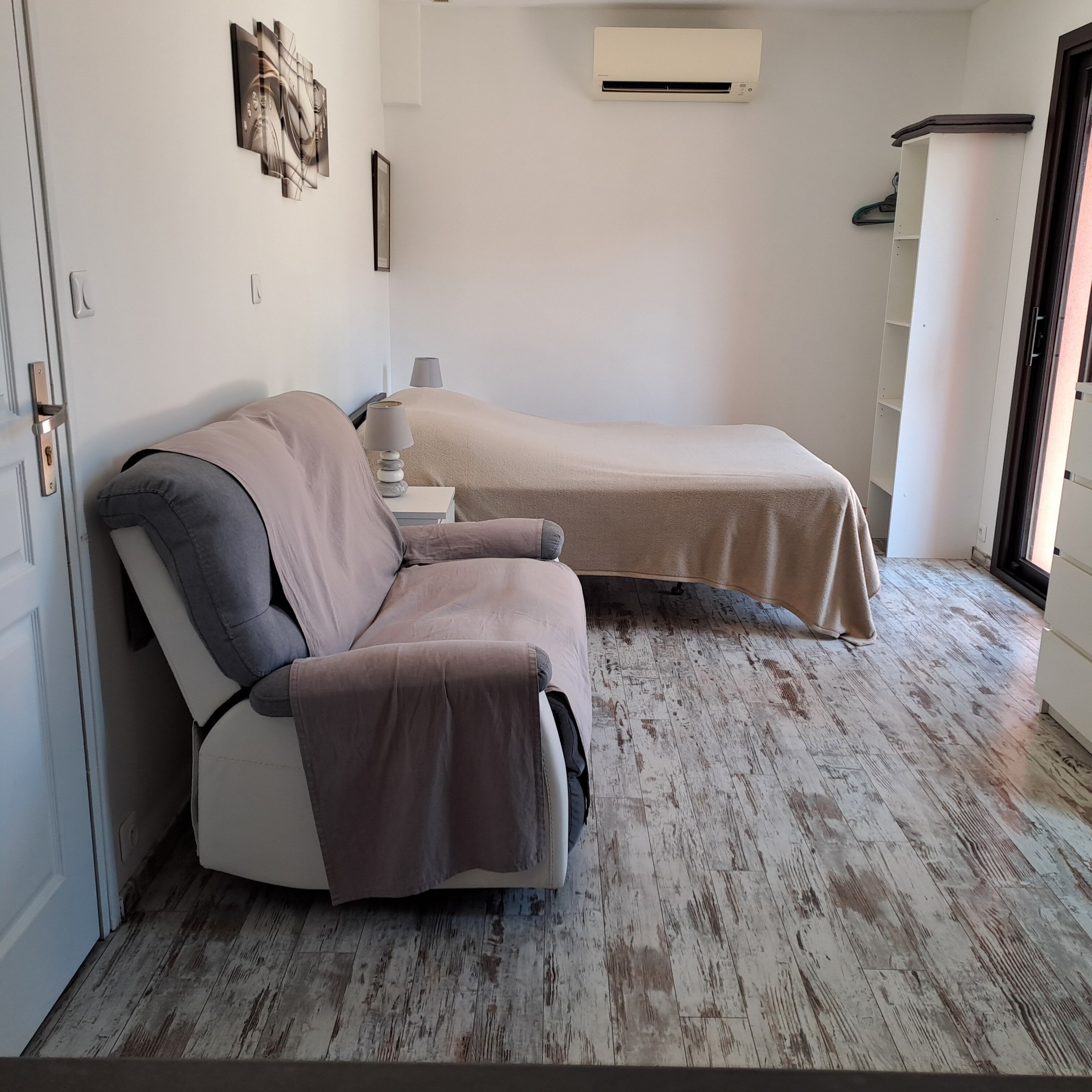 A room with a bed, a chair, a wall-mounted air conditioner, and a door.