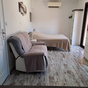 A room with a bed, a chair, a wall-mounted air conditioner, and a door. - A beautiful 3-star furnished room with air conditioning and a pool in L'Isle-sur-la-Sorgue (L'Isle-sur-la-Sorgue)