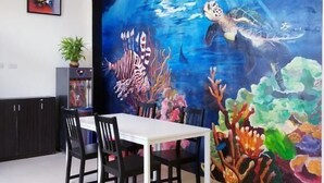 A dining area with a large mural of an underwater scene, a table, chairs, a potted plant, and a small aquarium. - Rainbow Homestay (Lyudao)