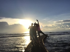 Een zonsondergang boven de oceaan, met mensen op een steiger.