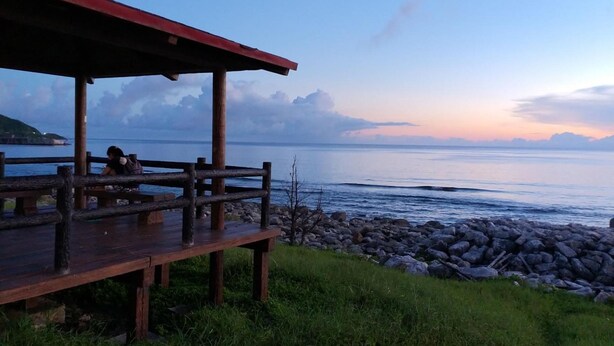 A wooden deck with a red roof overlooking a calm sea and rocky shoreline. - Rainbow Homestay (Lyudao)