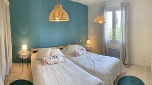Un letto matrimoniale con biancheria da letto bianca e cuscini decorativi, un comodino con lampada e un lampadario.