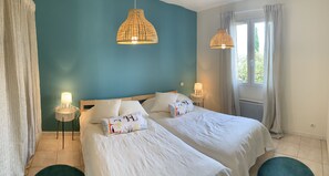 Ein Doppelbett mit weißer Bettwäsche und dekorativen Kissen, ein Nachttisch mit Lampe sowie eine Hängeleuchte.