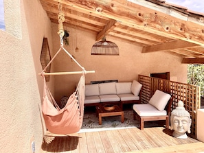 Eine Holzterrasse mit einer Hängesitzgelegenheit, einer Couch und einer Buddha-Statue.