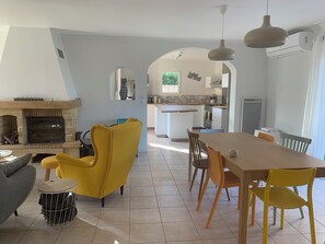 Ein modernes Wohnzimmer mit Kamin, gelbem Sessel und Essbereich mit Holztisch und Stühlen.