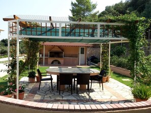 An outdoor patio with a round table and chairs, a grill, and a covered seating area. - Loggos view apartments (Kefalonia)