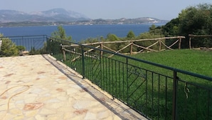A stone terrace with a metal railing overlooking a body of water and greenery. - Loggos view apartments (Kefalonia)