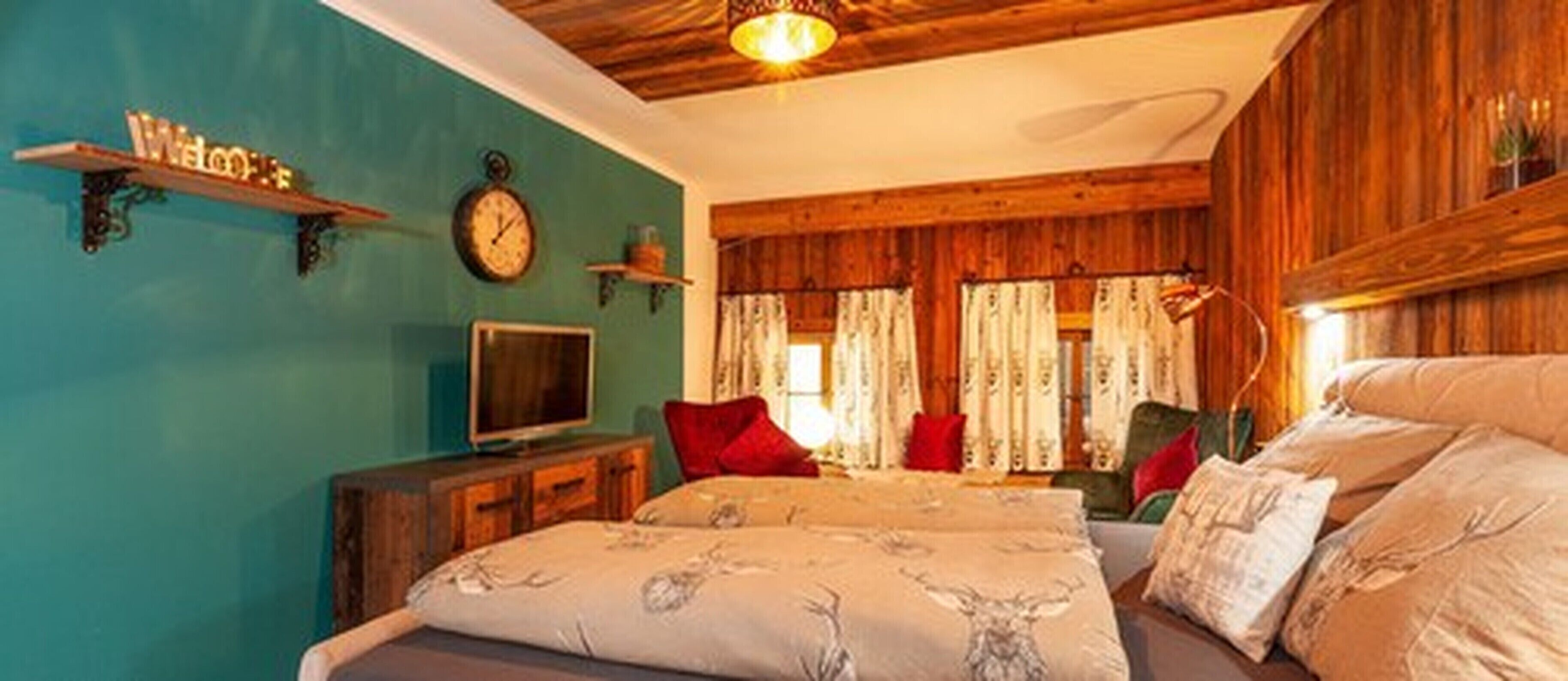 A cozy bedroom with a bed, a television, a clock, and wooden paneling on the walls.
