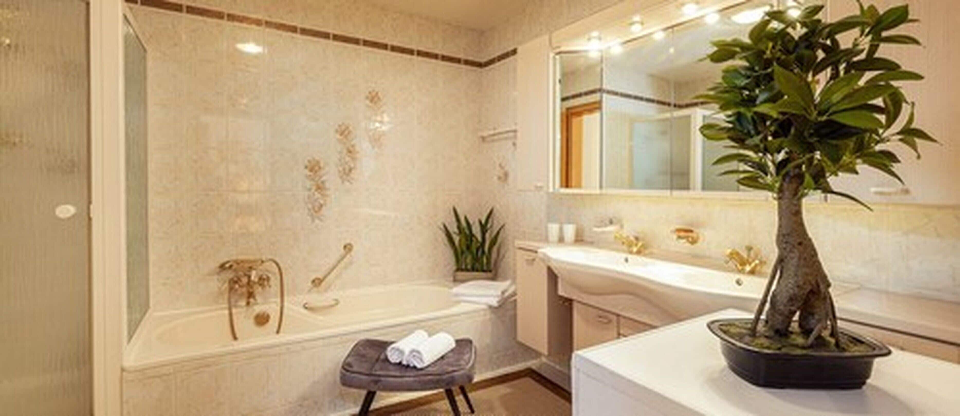 A modern bathroom with a bathtub, a sink, and a large mirror. There is a potted plant on the counter.