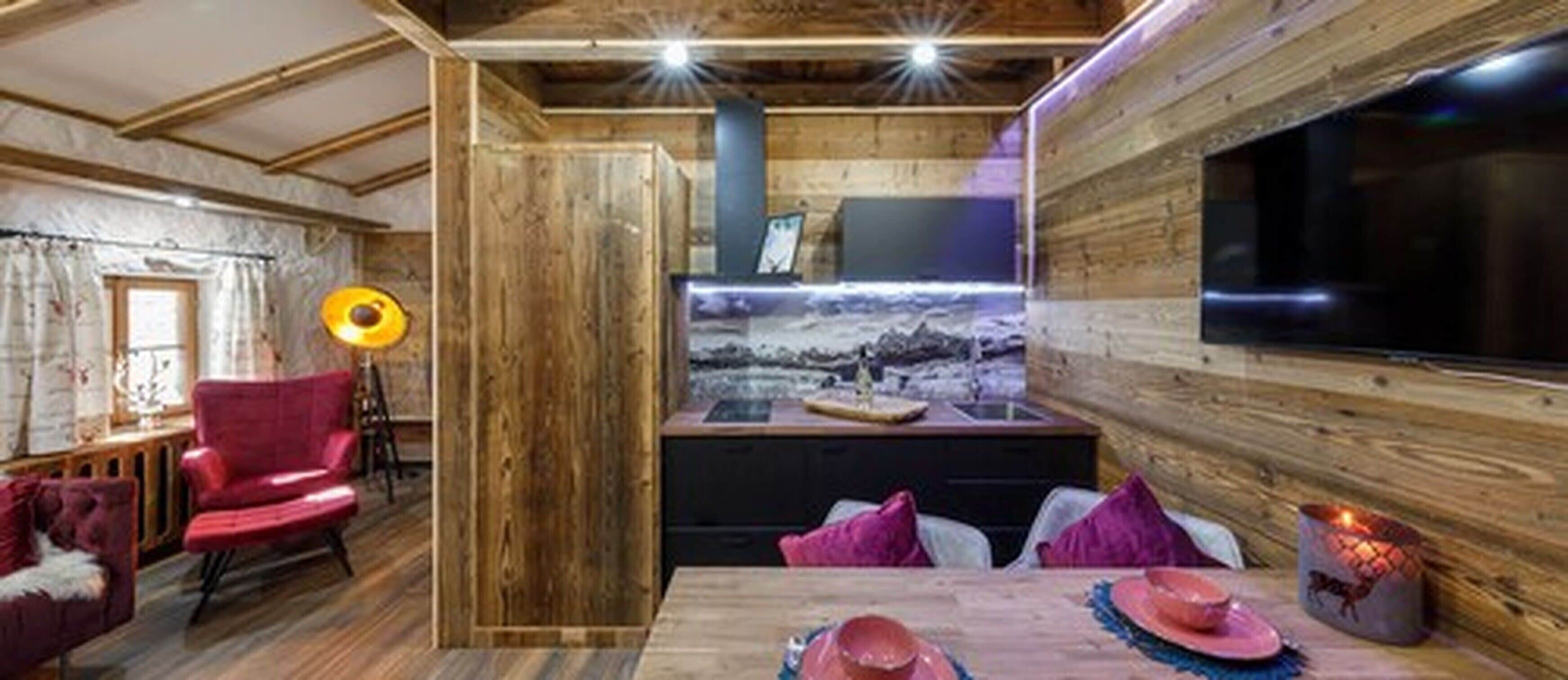 Een gezellige kamer met houten wanden, een grote flatscreen-tv, een open haard en een eethoek met een tafel gedekt voor twee personen.