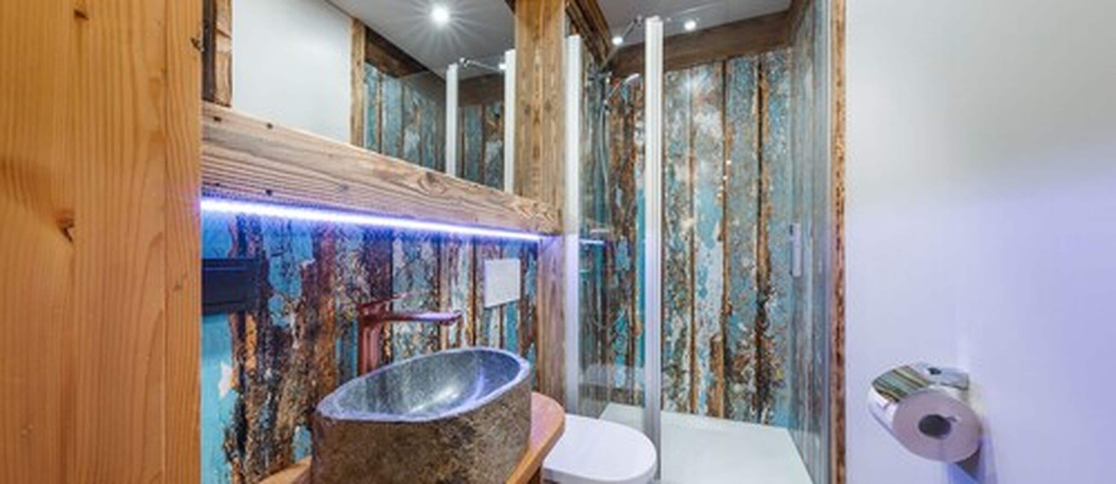 Ein Badezimmer mit rustikaler Holzvertäfelung, einem Steinwaschbecken und einer Glasdusche.