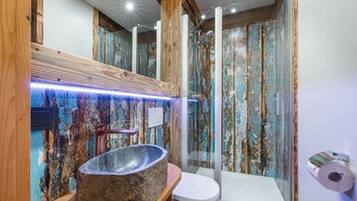 Ein Badezimmer mit rustikaler Holzvertäfelung, einem Steinwaschbecken und einer Glasdusche.