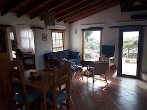 A cozy living room with a wooden dining table, blue upholstered chairs, a patterned sofa, and a television on a wooden stand. - CASA EL VALLITO YOUR PIECE OF HEAVEN AT EL HIERRO (Valverde)