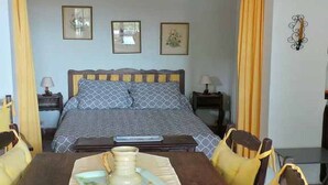 Una habitación con una cama, una mesa de comedor con sillas, una araña y cuadros enmarcados en la pared.