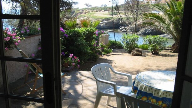 Un patio al aire libre con una mesa y sillas, rodeado de abundante vegetación y vistas a un lago.