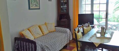 Una habitación con sofá, mesa de comedor, sillas, armario y ventana con cortinas.
