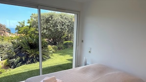 Ein Schlafzimmer mit großem Fenster, einem Bett mit gemustertem Überwurf und zwei Handtüchern auf dem Bett.