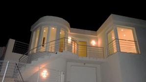 Ein modernes, zweistöckiges Haus mit einem geschwungenen Balkon, einer Treppe und einer Garage.