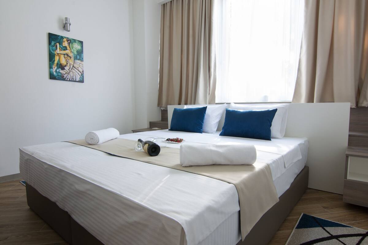 A neatly made bed with white linens, a rolled towel, and a pair of glasses on the bedside table.