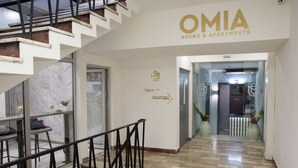 Interior de um hotel com escadaria, área de recepção e placas indicando o café e a recepção.