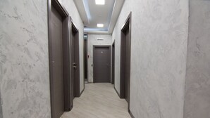 Corredor com paredes de mármore e portas de madeira, que leva a uma porta central.