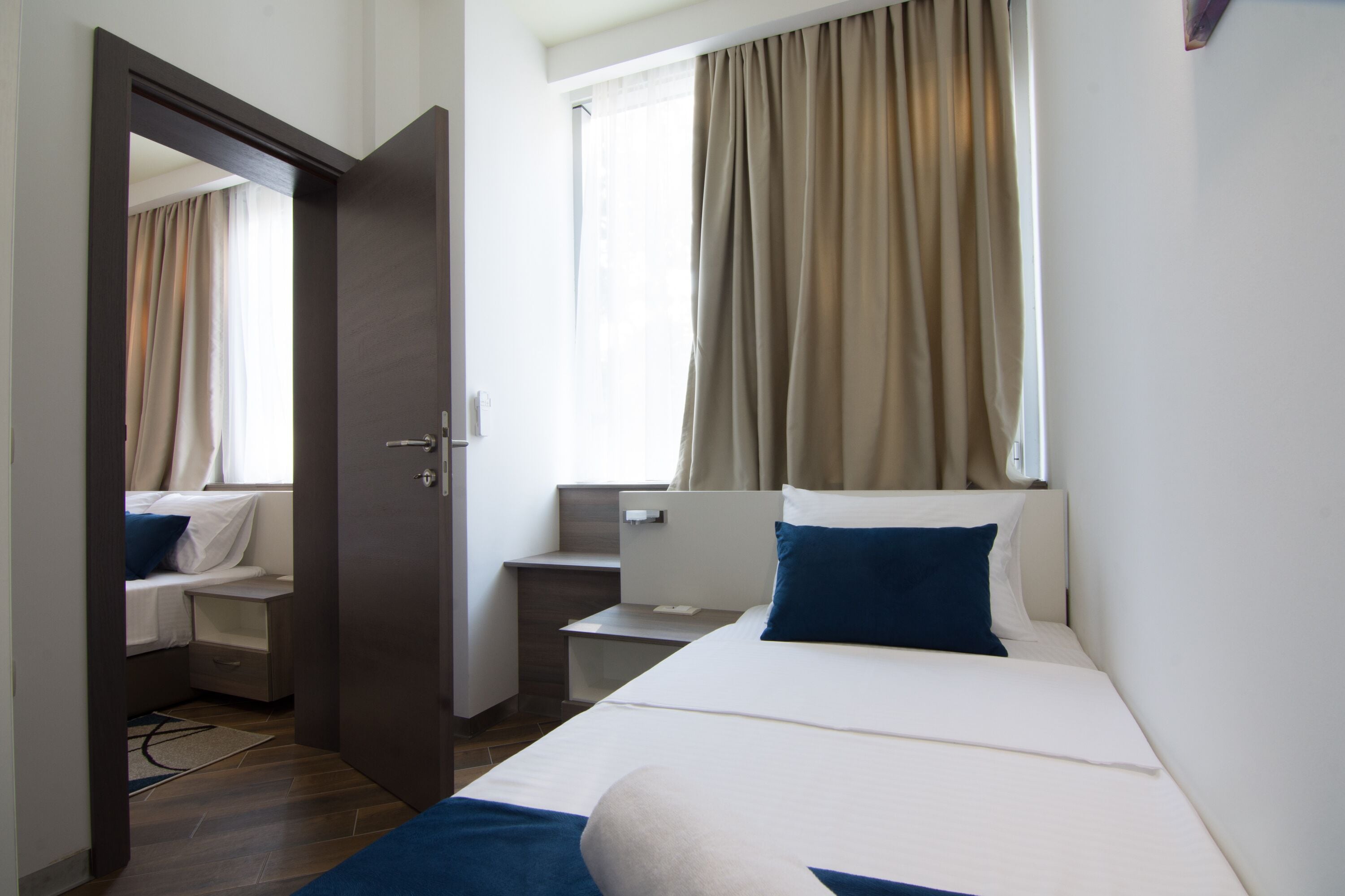 A hotel room with a bed, a desk, a chair, a window with curtains, and a door.