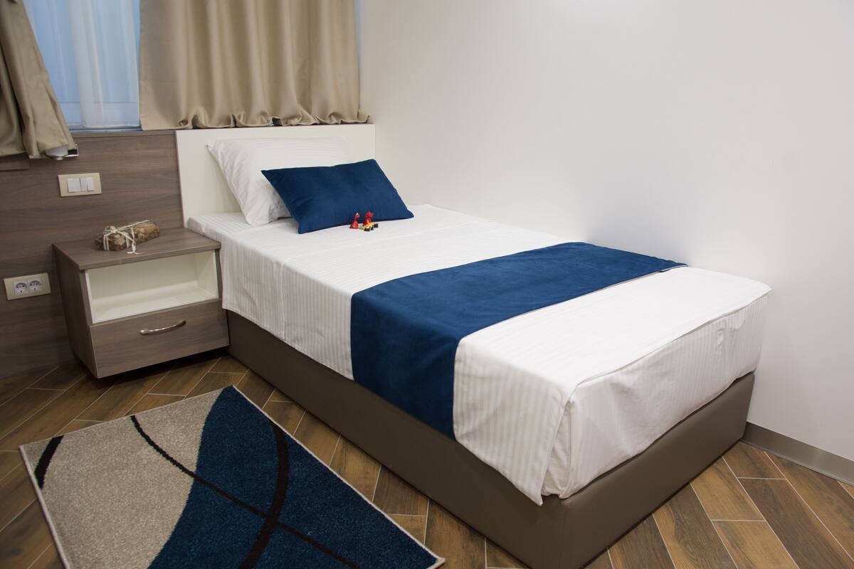 A neatly arranged hotel room with a bed, bedside table, and a small drawer unit.