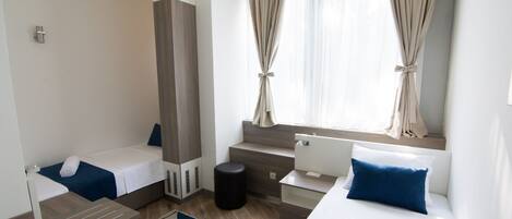 A hotel room with two beds, a desk, a small stool, and a window with curtains.