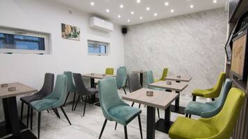 Interior de un restaurante con varias mesas y sillas, suelo de mármol e iluminación empotrada en el techo.