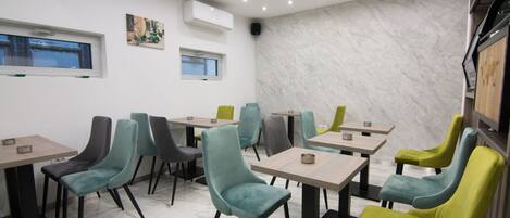Interior de un restaurante con varias mesas y sillas, suelo de mármol e iluminación empotrada en el techo.