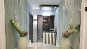 Uma área de recepção moderna com balcão, paredes de vidro e vasos decorativos com flores.