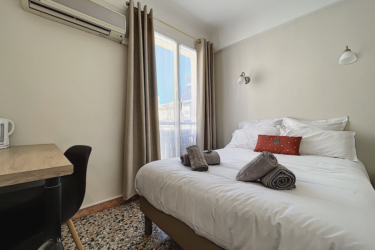 A hotel room with a bed, a desk, a chair, and a window with curtains.