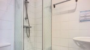 Une salle de bain avec une douche à parois de verre, un lavabo blanc et un petit tabouret.