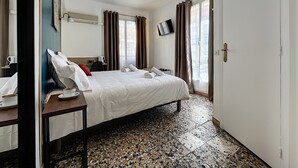 Une chambre d’hôtel comprenant un lit, un bureau avec une chaise, une télévision et une fenêtre avec des rideaux.