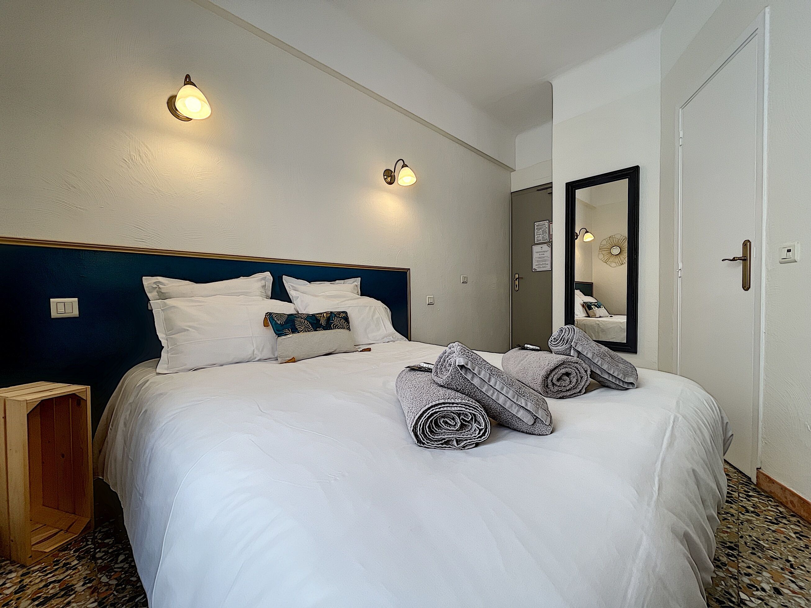A hotel room with a neatly made bed, two wall-mounted lights, a wooden side table, and a mirror on the wall.