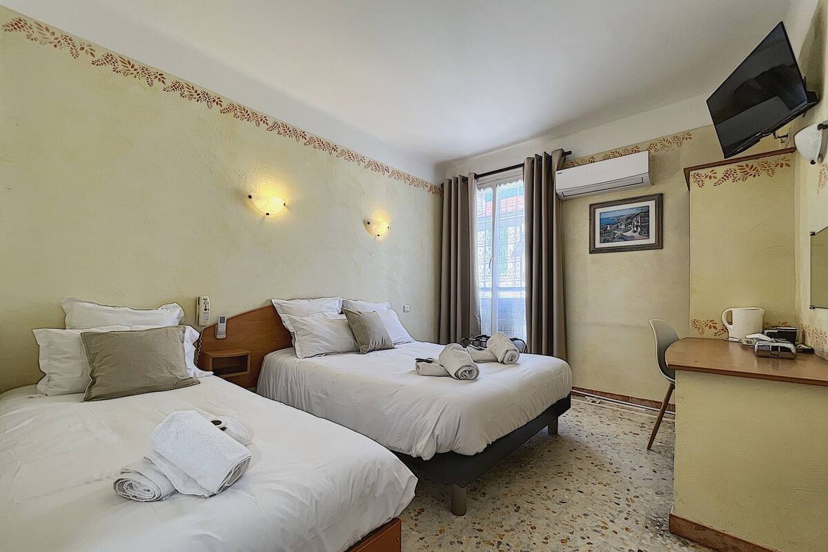 A hotel room with two beds, a desk, a TV, and a window with curtains.