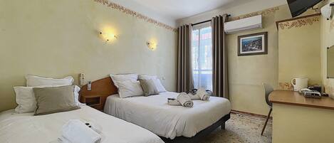Une chambre d’hôtel avec deux lits, un bureau, une télévision et une fenêtre avec des rideaux.