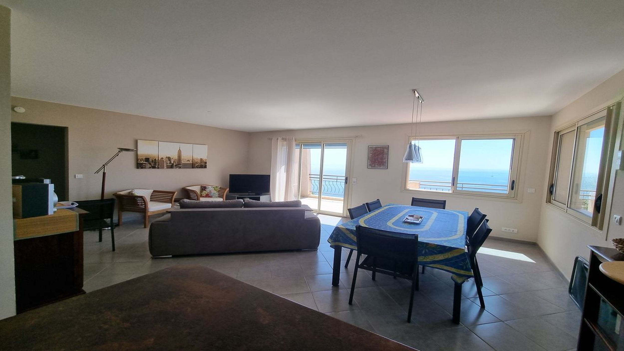 A spacious living area with a dining table, sofas, and a balcony with a view of the sea.