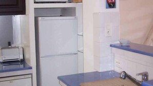 A compact kitchen with a microwave, refrigerator, and a sink with a cutting board. - La Calanque 263 villa (Les Issambres)