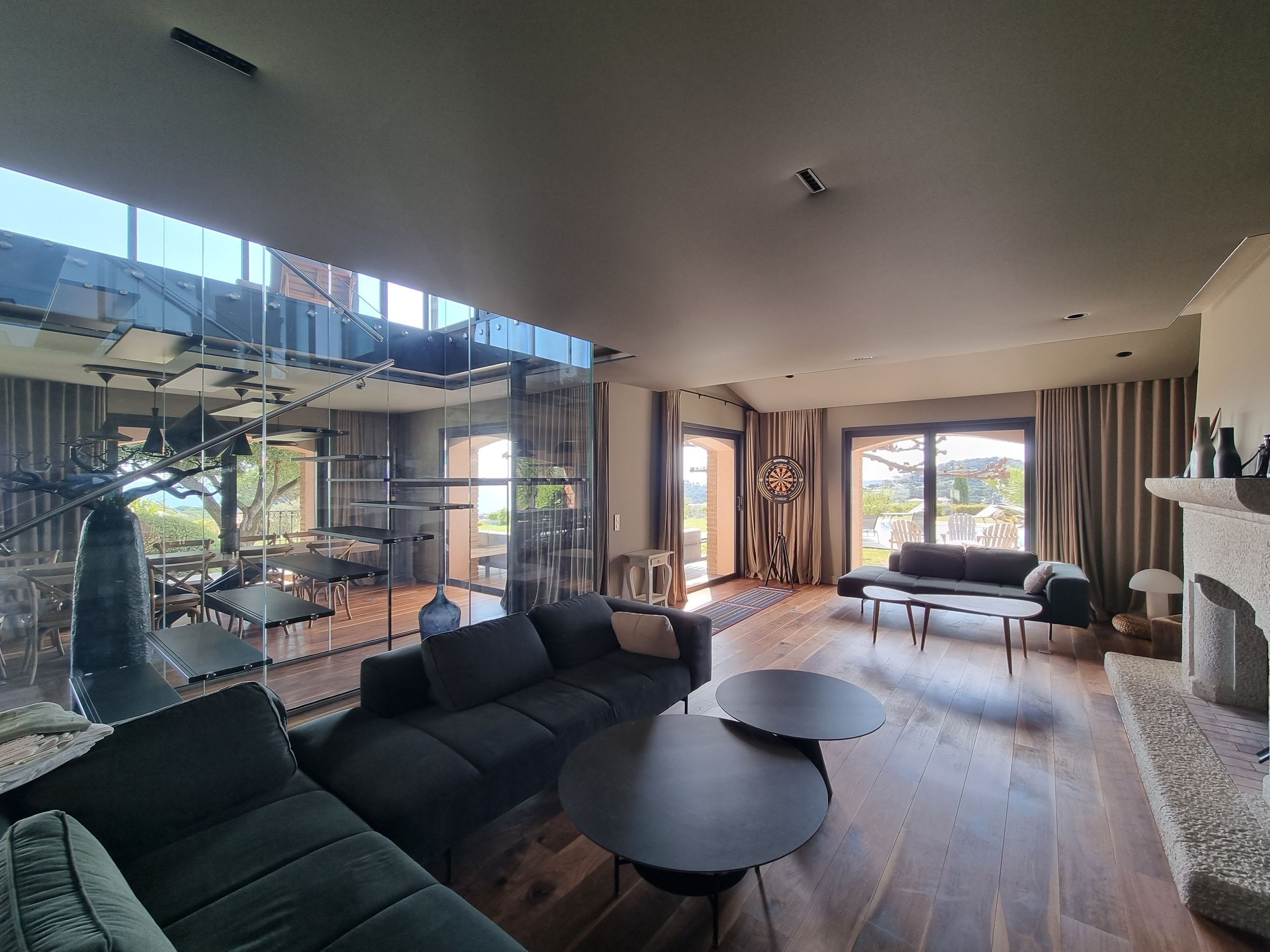 A spacious living area with a modern design, featuring a sectional sofa, two round coffee tables, and a large window offering a view of the outdoors.