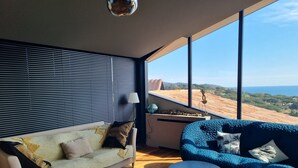 A modern living room with a sofa and a blue armchair, a round coffee table, and a large window offering a view of the countryside. - Pierre Jean 1823 villa (Sainte-Maxime)