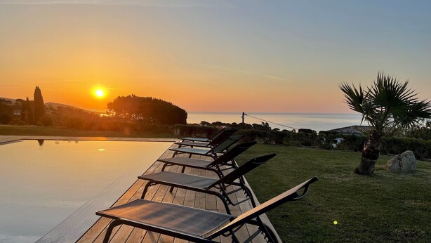 A wooden deck with lounge chairs overlooking a swimming pool at sunset. - Pierre Jean 1823 villa (Sainte-Maxime)