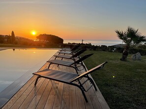 A wooden deck with lounge chairs overlooking a swimming pool at sunset.