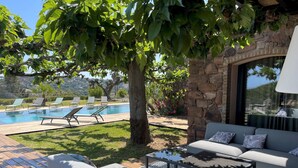 A poolside area with a stone wall, a sofa, and lounge chairs. - Pierre Jean 1823 villa (Sainte-Maxime)