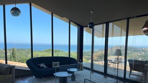 A modern living room with a large window overlooking a scenic view of the sea and greenery. - Pierre Jean 1823 villa (Sainte-Maxime)