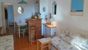 Een compacte leefruimte met een eethoek, een bank met marine behang, een kleine tafel met een lamp en een wandspiegel.