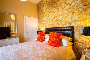 Quarto de hotel com cama, televisão e papel de parede floral.