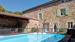 A stone building with a swimming pool, outdoor seating, and a wooden deck.