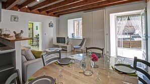 A dining area with a wooden table set for four, a television, and a view of a garden through a window.