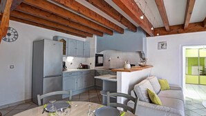 A kitchen with wooden beams, a dining table set for four, and a grey sofa in the living area.